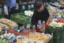 Austria, Vienna, The Naschmarkt, Stallholder selecting mushrooms from display of fresh produce also including potatoes, tomatoes and squash.