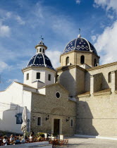 Spain, Costa Blanca, Valencia, Alicante Province, Altea, Church with blue tiled roof in the square with tourists sat outsde cafe.