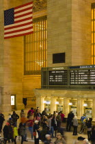 USA, New York, Manhattan, Grand Central Terminus railway station with passengers buying tickets from ticket booths in the Main Concourse beneath the American Stars and Stripes flag hanging from the ce...