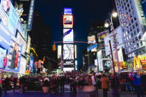 USA, New York, Manhattan, People walking at night in Times Square at the junction of 7th Avenue and Broadway below buildings with advertising on large video screens.