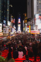 USA, New York, Manhattan, People sitting on lit red steps or walking at night in Times Square at the junction of 7th Avenue and Broadway below buildings with advertising on large video screens.