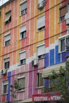 Albania, Tirane, Tirana, Part view of exterior facade of apartment block painted in brightly coloured stripes with multiple windows. Sign for Tristar Studio, video and internet business below.