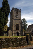 England, Devon, Norman church clock tower and entrance throfugh graveyard.