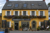 Ireland, County Cork, Kinsale, Bulman public house painted yellow with couple sat outside.