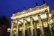 Mexico, Bajio, Guanajuato, Illuminated exterior facade of Theatre Juarez with line of rooftop statues at night.