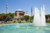 Turkey, Istanbul, Sultanahmet, Haghia Sophia with dome and minarets beyond the water fountain in the gardens with sightseeing tourists.