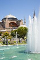 Turkey, Istanbul, Sultanahmet, Haghia Sophia with dome and minarets beyond the water fountain in the gardens with sightseeing tourists.