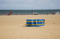 England, Lincolnshire, Skegness, Lincs Wind Farm offshore on the horizon with families and windbreaks on the beach.