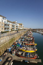 England, East Sussex, Brighton, view over fishing boats moored in the Marina with apartment buildings behind.