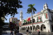 Mexico, Veracruz, The zocalo and government buildings decorated for Independence Day celebrations, with balloon seller and tourists in the foreground, part framed by tree.