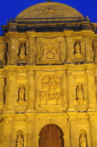 Mexico, Oaxaca, Part view of baroque exterior facade of cathedral at night with relief carving of the assumption of the Virgin Mary above door.