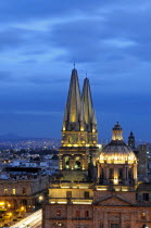 Mexico, Jalisco, Guadalajara, Cathedral domed roof and bell towers at night with city spread out behind.