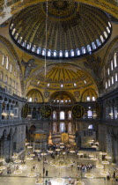 Turkey, Istanbul, Sultanahmet, Haghia Sophia Sighseeing tourists beneath the dome with murals and chandeliers in the Nave of the Cathedral.