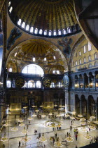 Turkey, Istanbul, Sultanahmet, Haghia Sophia Sighseeing tourists beneath the dome with murals and chandeliers in the Nave of the Cathedral.