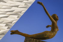 Ireland, Belfast, Titanic Quarter, Titanic Belfast Visitor Experience, 'Titanica' sculpture by Rowan Gillespie with a section of the building and blue sky in the background.