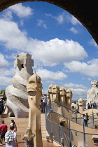 Spain, catalonia, Barcelona, Tourist visitors amongst the chimneys and vents on the roof of Casa Mila apartment building known as La Pedrera or Stone Quarry designed by Antoni Gaudi in the Eixample di...