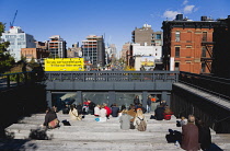 USA, New York, Manhattan, people seated on the the 10th Avenue Square viewing platform on the High Line a linear park on an elevated disused section of railroad looking at traffic on the road below.