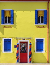 Italy, Veneto, Burano Island, Yellow house facade on Fondamenta della Giudecca with colourful red door and blue shutters.