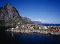 Norway, Lofoten, Moskenesoya Island, Hamnoy fishing village.  Red  white and green painted houses on rocky promontory with Festhaeltinden Mountain on left behind.