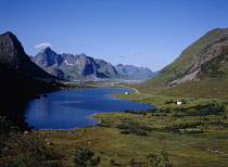 Norway, Lofoten, Storvatnet Lake, View across lake west of the village of Napp with Flakstadtinden mountain behind with single cloud drifting across peak.