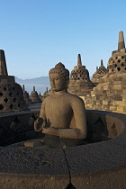 Indonesia, Java, Borobudur, Seated Buddha on the top level lit by early-morning, warm sun, surrounded by stupas