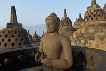 Indonesia, Java, Borobudur, Seated Buddha on the top level lit by early-morning, warm sun, surrounded by stupas