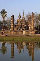 Thailand, Sukothai, Seated Buddha and stupa reflected in a pond at sunset, Wat Mahathat Royal Temple.