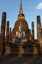 Thailand, Sukothai, Seated white Buddha in front of red brick stupa, both lit by the warm sunset light, Wat Sra Sri.