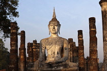 Thailand, Sukothai, White seated Buddha, with pillars either side of him, lit at sunset, Wat Mahathat Royal Temple.