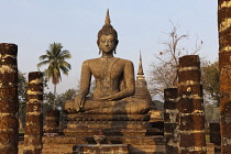 Thailand, Sukothai, Seated Buddha on a plinth, with stupa in the background, lit by the warm light at sunset, Wat Mahathat Royal Temple.