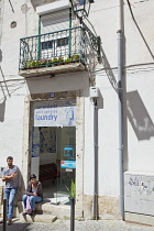 Portugal, Estredmadura, Lisbon, Alfama district, Man and woman sat outside laundromat.