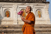 India, Bihar, Bodhgaya, A Buddhist monk holding lotus flowers prays at the Mahabodhi Temple in Bodh.