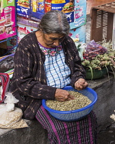 Guatemala, Solola Department, Santiago Atitlan, A Mayan woman wearing traditional dress sorts nuts for sale in the market.