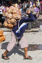 Guatemala, Solola Department, Santiago Atitlan, A young man carries a heavy load of oranges from the market on his back using a tumpline.