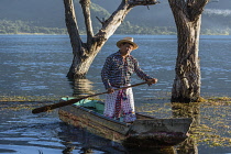 A Tzutujil Mayan man in the traditional dress of San Pedro la Laguna paddles his cayuco or fishing canoe on Lake Atitilan in Guatemala.
