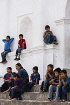 Guatemala, Solola Department, San Antonio Palopo, A Cakchiquel Mayan woman and children watch a program from the steps of the church. The woman and girls wear the traditional dress of San Antonio Palo...