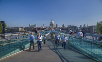 England, London, City workers crossing the Millennium Bridge with the dome of St Paul's Cathedral in the background.