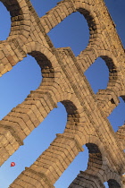 Spain, Castile and Leon, Segovia, Hot air balloon gliding past as early morning golden light shines on the Aqueduct of Segovia, a Roman aqueduct with 167 arches built around the first century AD to ch...