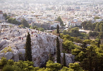 Greece, Attica, Athens, tourists on rocks below the acropolis overlooking odeon of herodes atticus and city.