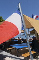 France, Provence-Alpes-Cote d'Azur, Antibes, Tricolour flag flying poutside beach front cafe with Cap d'Antibes visible in the background.