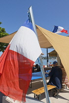 France, Provence-Alpes-Cote d'Azur, Antibes, Tricolour flag flying poutside beach front cafe with Cap d'Antibes visible in the background.