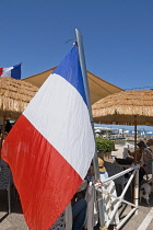 France, Provence-Alpes-Cote d'Azur, Antibes, Tricolour flag flying poutside beach front cafe.