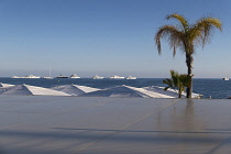 France, Provence-Alpes-Cote d'Azur, Antibes, Juan-les-Pins, View over beach front parasols towards yachts moored offshore.