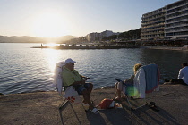 France, Provence-Alpes-Cote d'Azur, Antibes, Juan-les-Pins, People sat on chairs enjoying the sunset from the jetty.