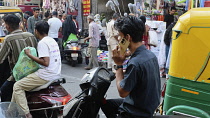 India, Gujarat, Ahmedabad, Market, man using mobile phone whilst sat on moped.