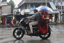 India, Tamil Nadu, Nandyal, People on motorbikes holding umbrellas during monsoon.