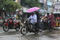 India, Tamil Nadu, Nandyal, People on motorbikes holding umbrellas during monsoon.