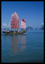 Thailand, Phuket Province; Tourist excursion on Chinese junk with pink sails reflected in deep aquamarine water.